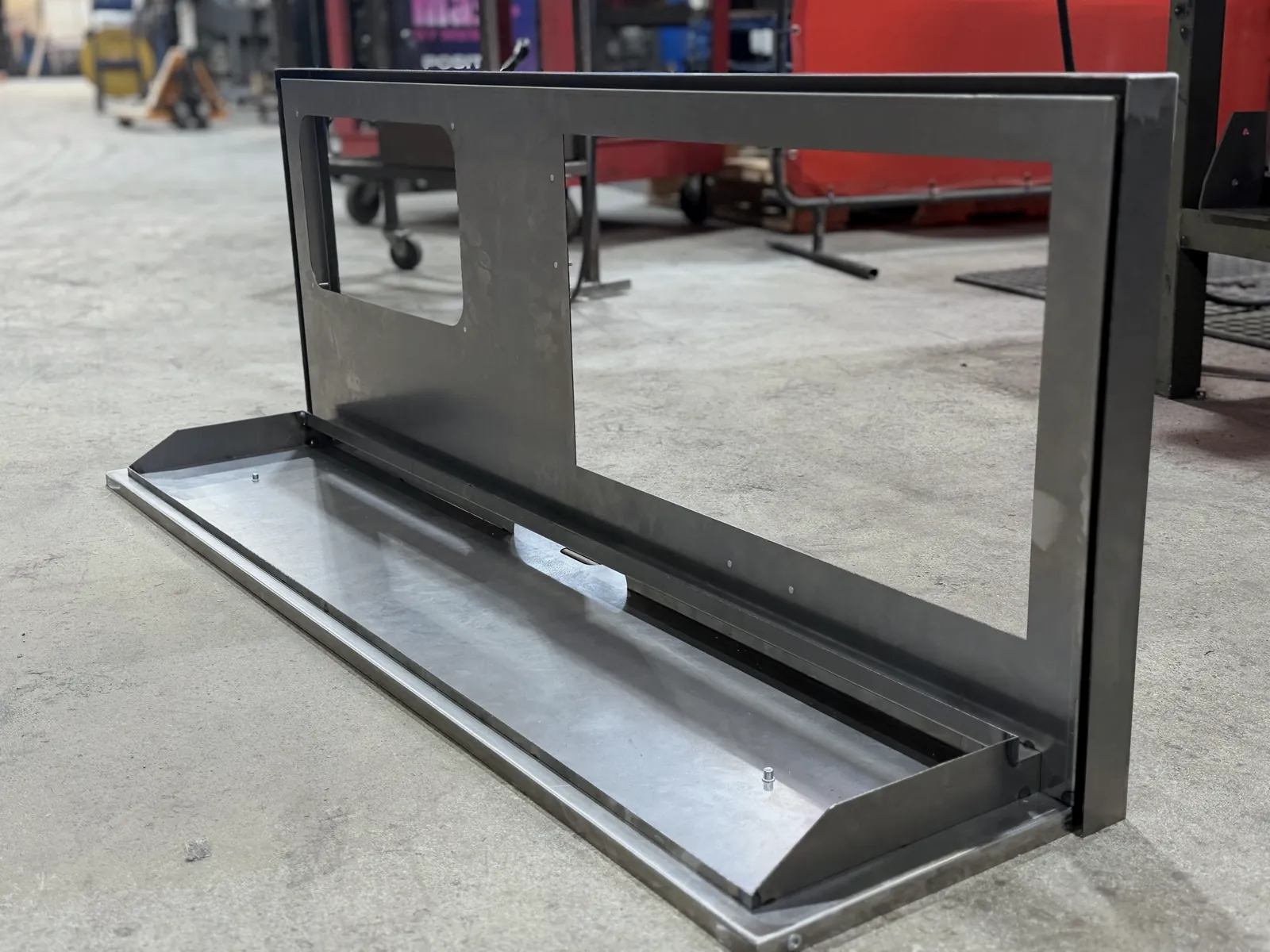 Long countertop camera display holder in raw steel, with cut-out back panel and angled front tray