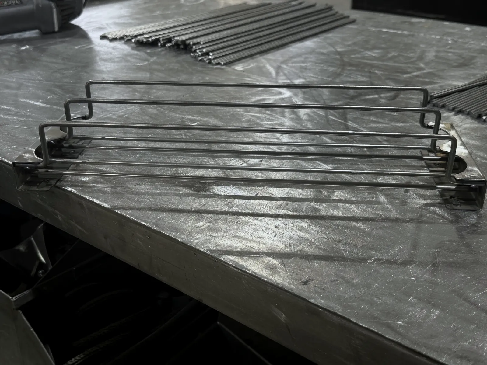 Single wire drink shelf pusher on the workbench, with bundled wire stock behind it